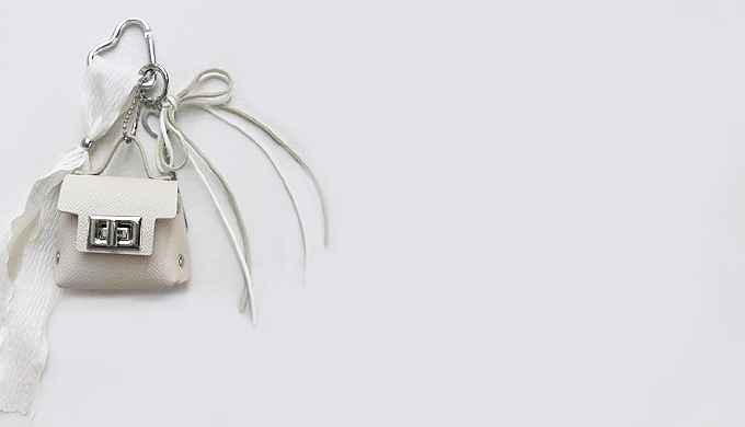 A mini bag-shaped charm keyring with a carabiner and ribbon decoration, perfect for attaching to bag...