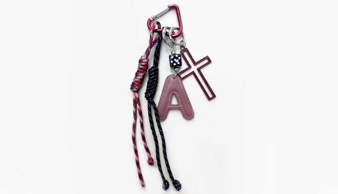 Stylish cross charm keyring with unique details such as an initial A, black cross, and astronaut pen...